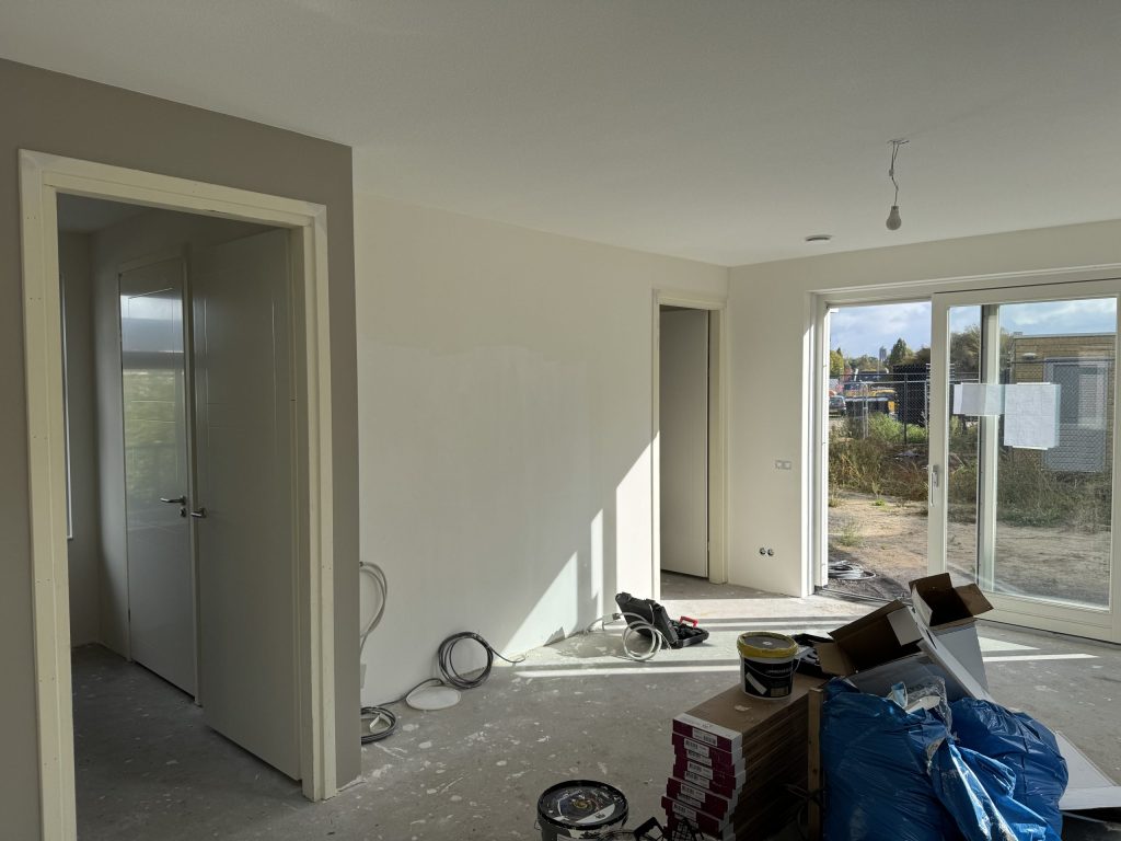 Kamer in een nieuwe woning met gladde wanden, openslaande deuren en materiaal op de vloer
