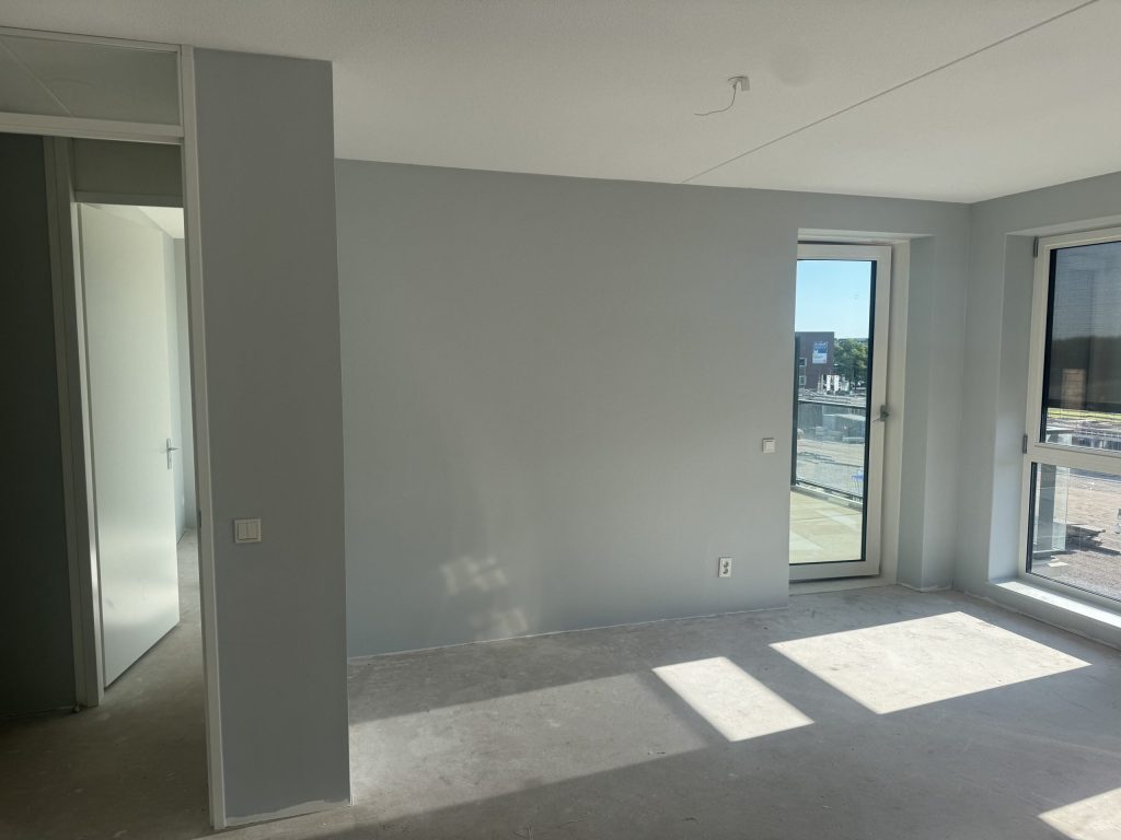 Lichte kamer met grijze wanden, een balkondeur en een kale betonvloer