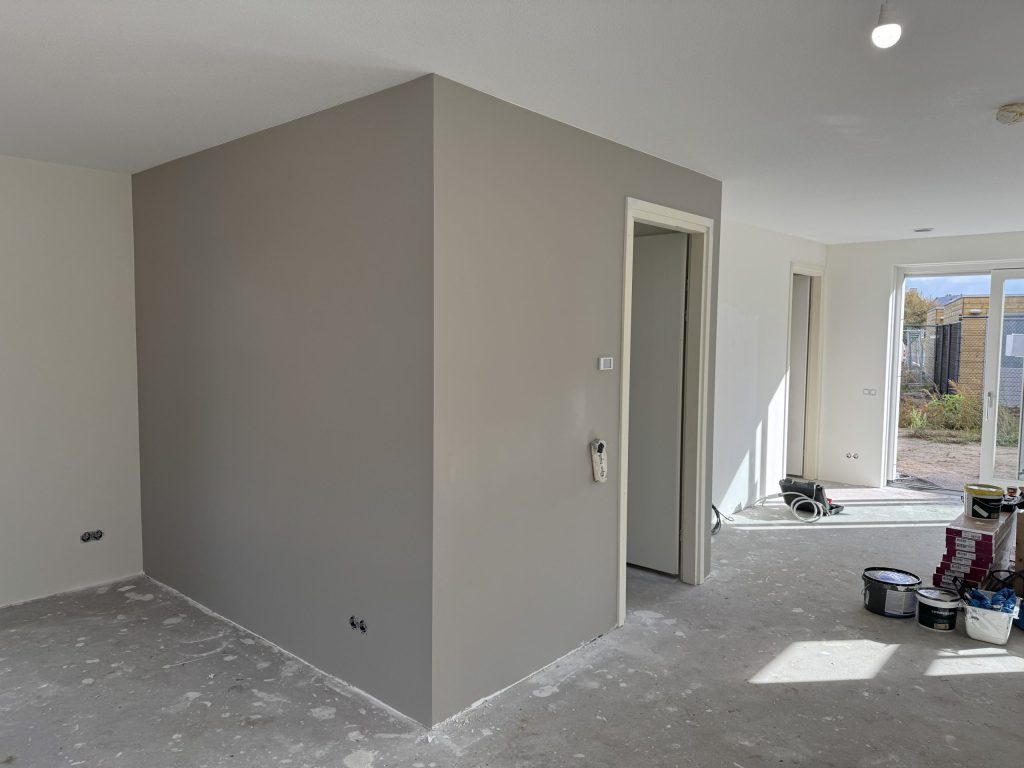 Woonkamer met een pas gesausde grijze wand en verfemmers op de betonvloer